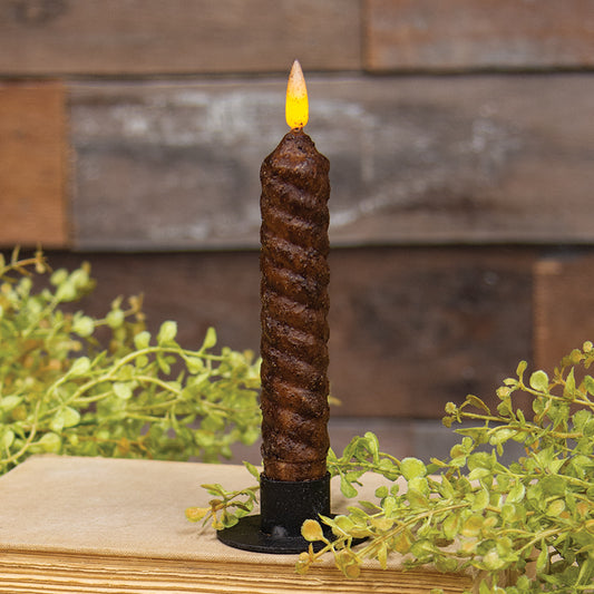 A burnt mustard colored vintage-style flameless candle with a twist flicker flame, placed on a wooden surface with greenery in the background.