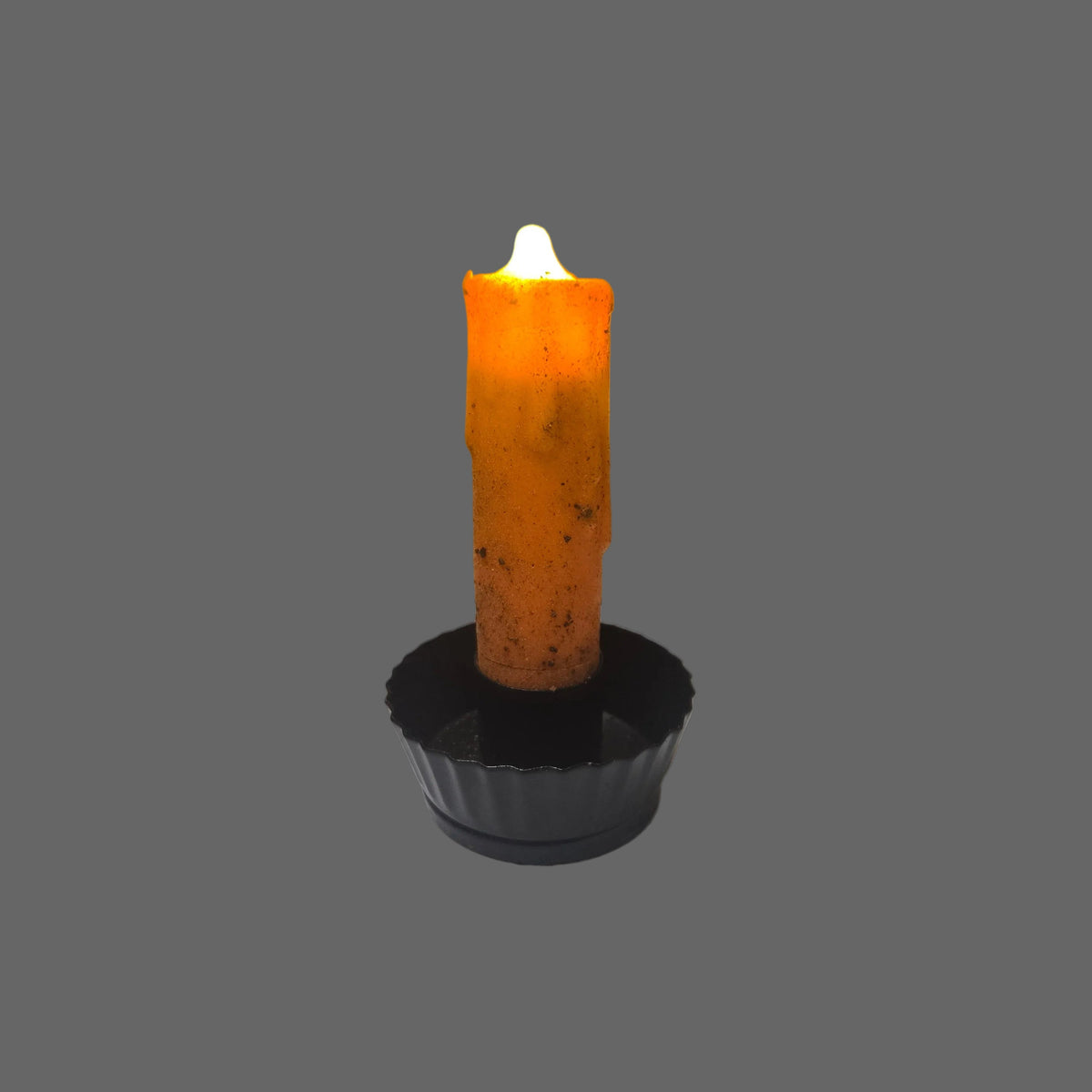 An orange taper candle with a textured, melted wax finish, lit with a small white flame, set in a black cup holder against a solid gray background.