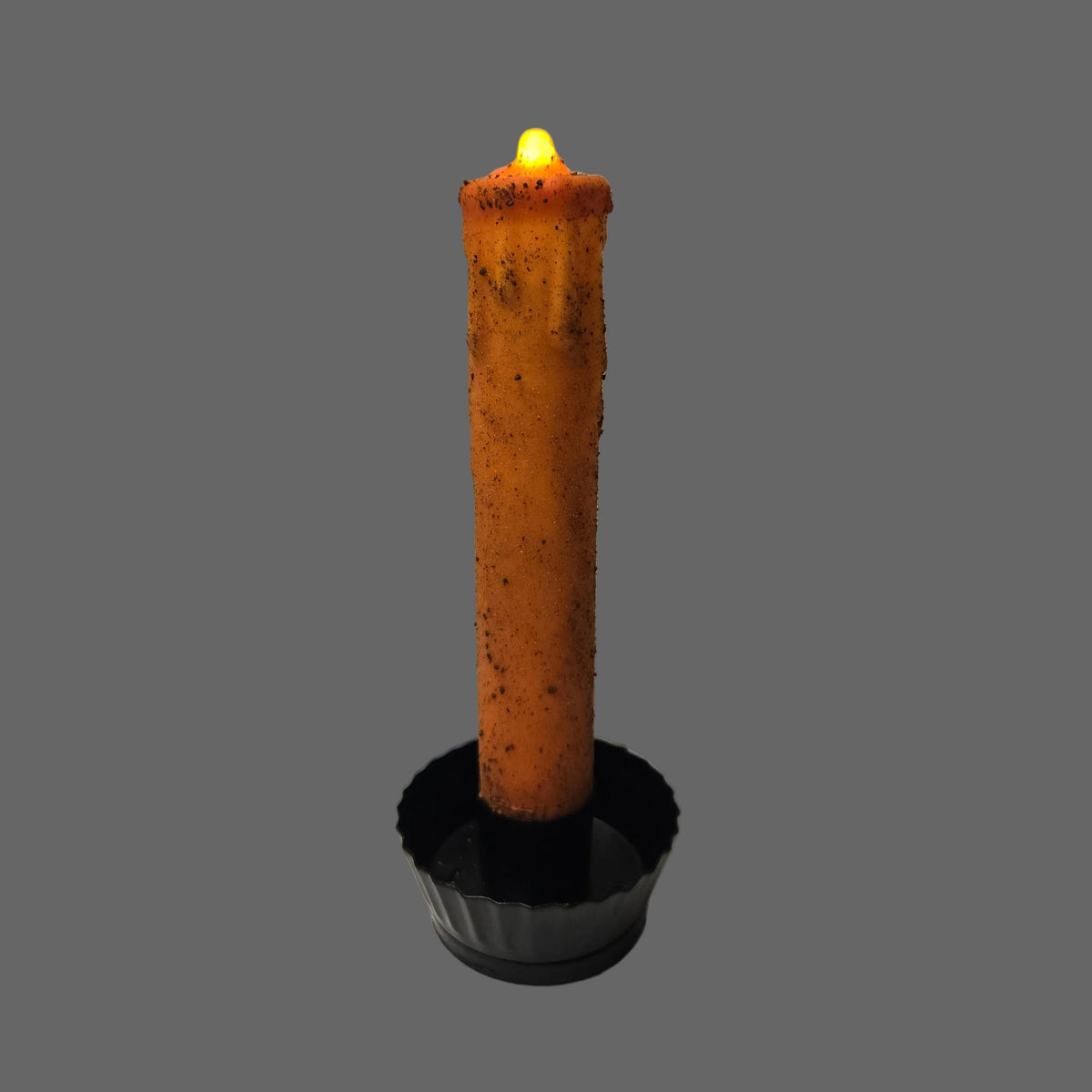 A single orange-brown wax candle with a black base, shown lit with a small yellow flame against a plain light gray background.
