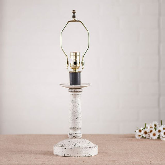 Wooden lamp base with white paint on white background with daisies beside it