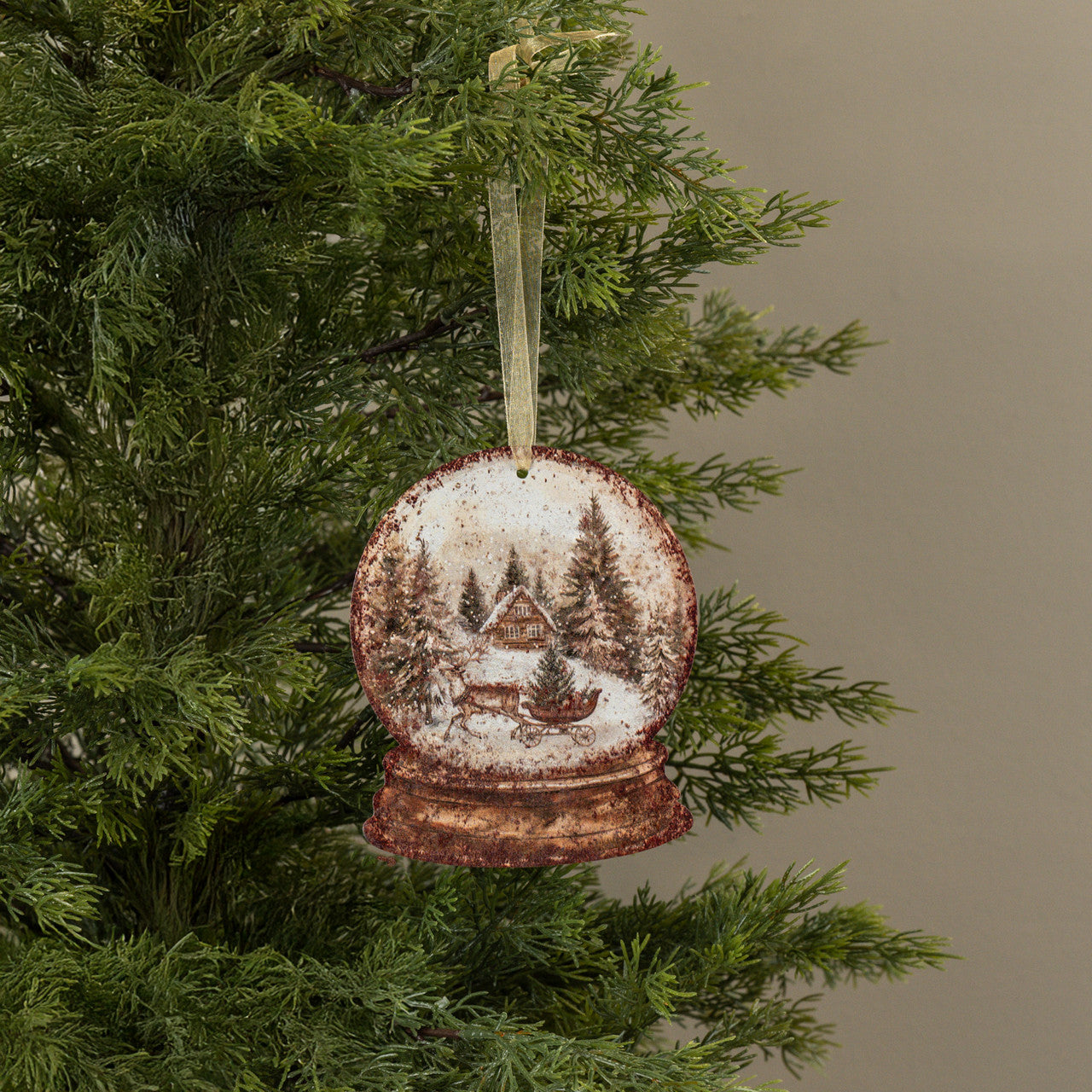 Christmas ornament shaped like a snow globe with a cabin and trees on a tree branch.