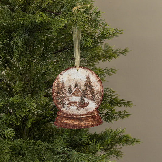Christmas ornament shaped like a snow globe with a cabin and trees on a tree branch.
