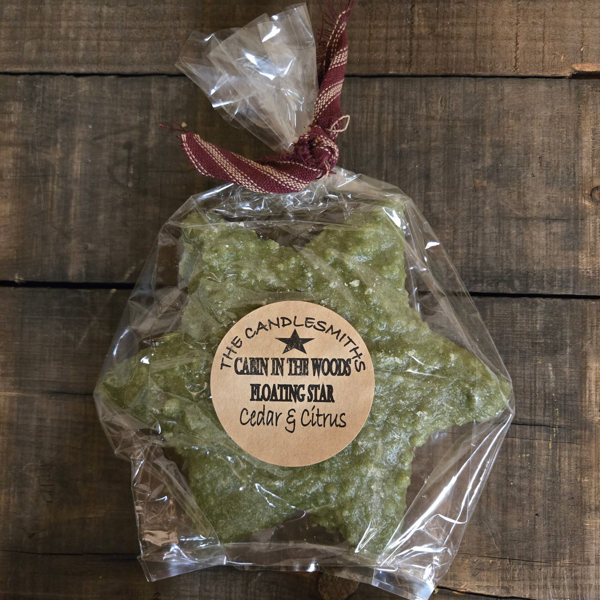 Cabin in the Woods green star floating candle in clear wrapping with burgundy ribbon and a Cedar & Citrus label.