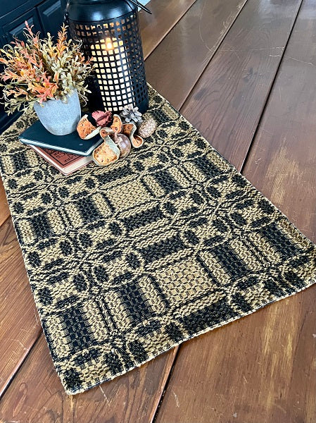A mustard and black long table runner displayed on a wooden table with a decorative centerpiece.