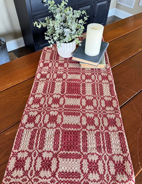 A red and tan short table runner with a geometric pattern laid out on a wooden table.