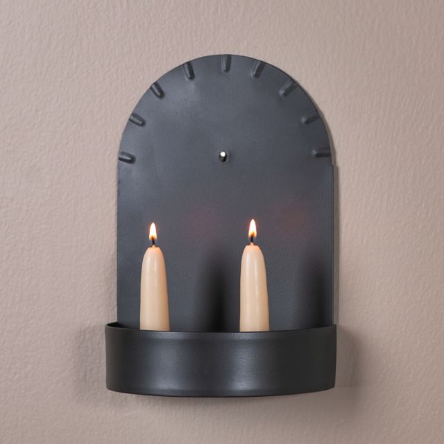 Black wall-mounted candle holder with two lit candles on a beige wall.