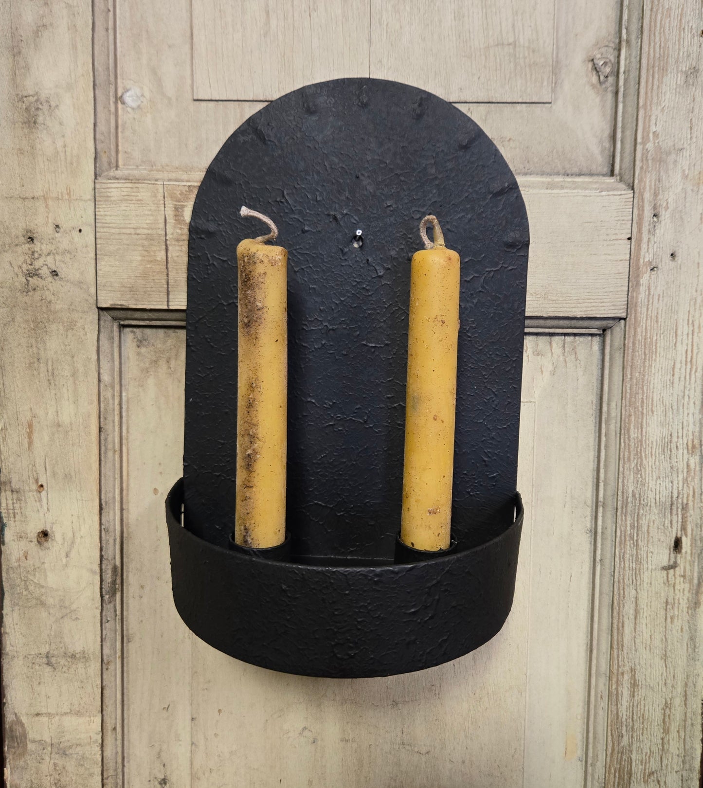 Black wall-mounted candle holder with two yellow candles on a wooden background