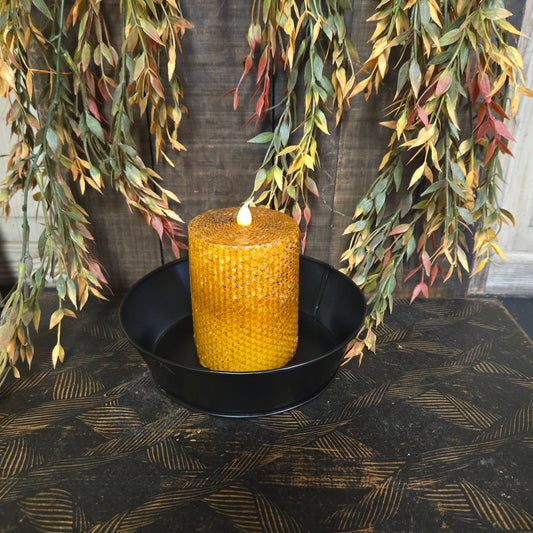 Yellow candle in a black holder on a textured surface with leaves