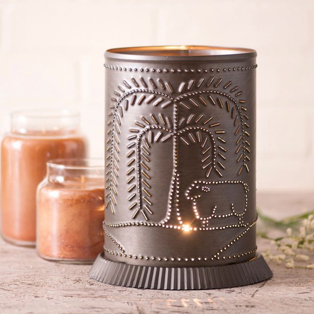 Decorative wax warmer with tree and sheep design on a wooden surface with candles in the background.