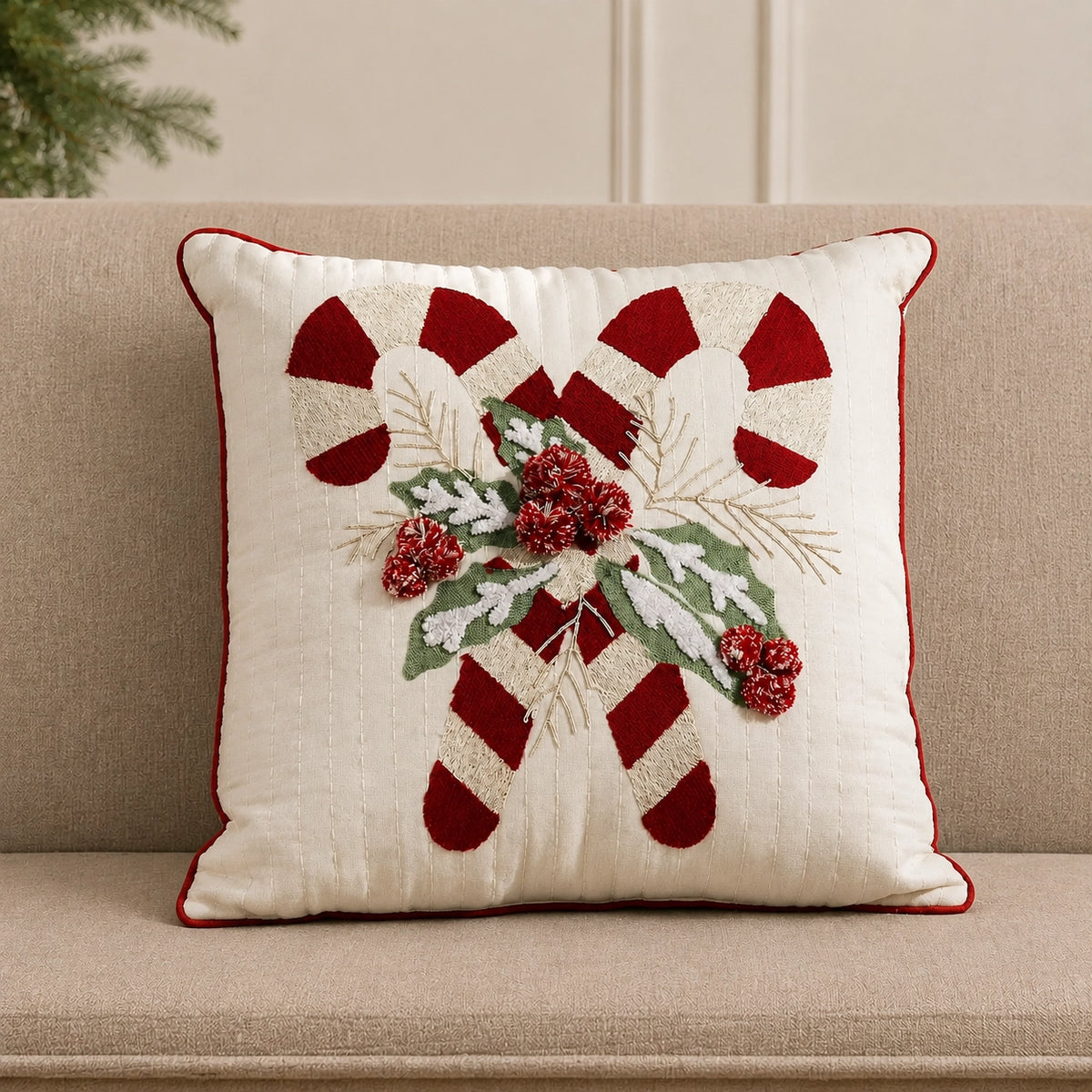 Cream Christmas throw pillow with crossed red-and-white candy canes, snowy holly leaves, red berries and red piping on a beige sofa.