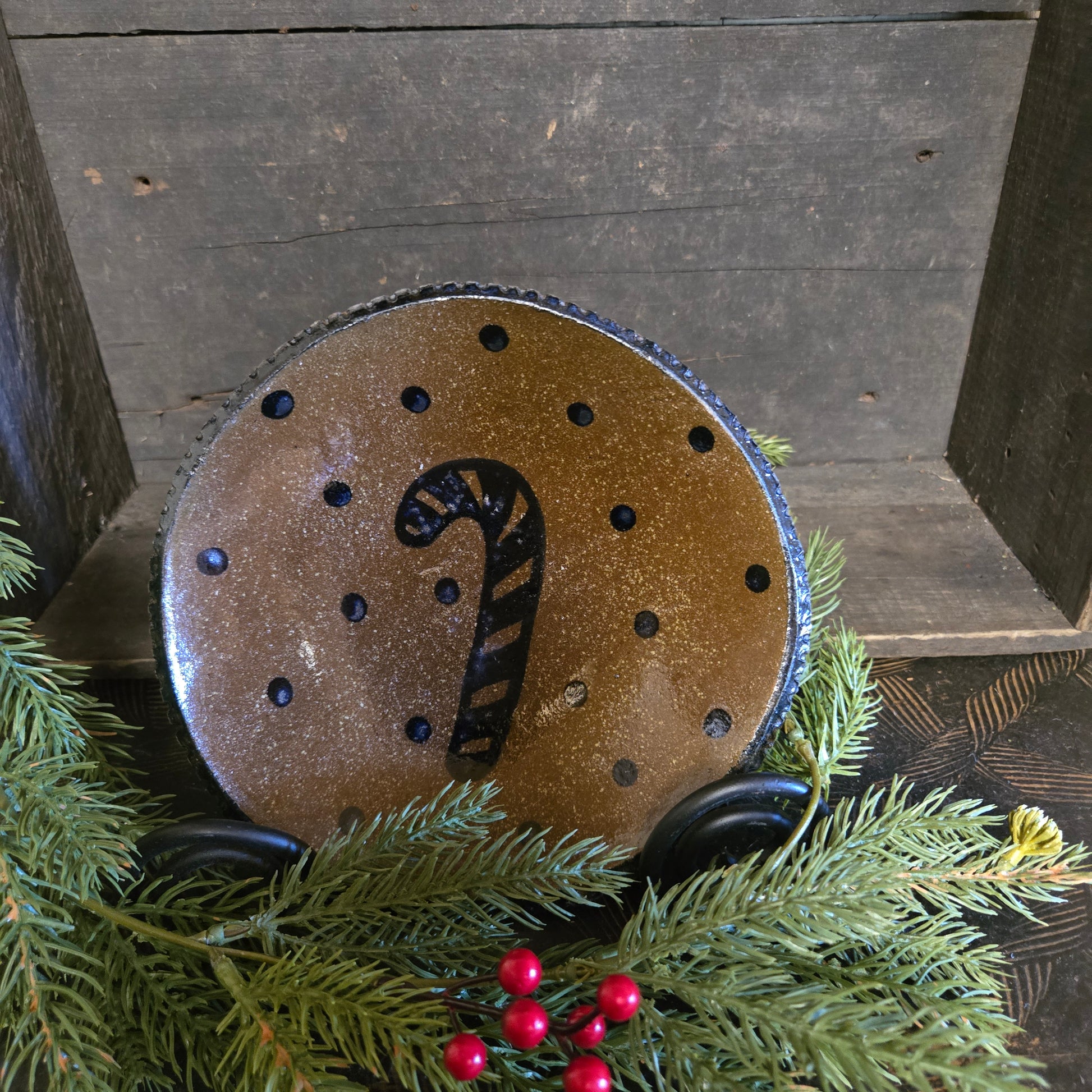 Decorative stoneware plate with a candy cane design on a wooden surface with greenery