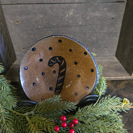 Decorative stoneware plate with a candy cane design on a wooden surface with greenery