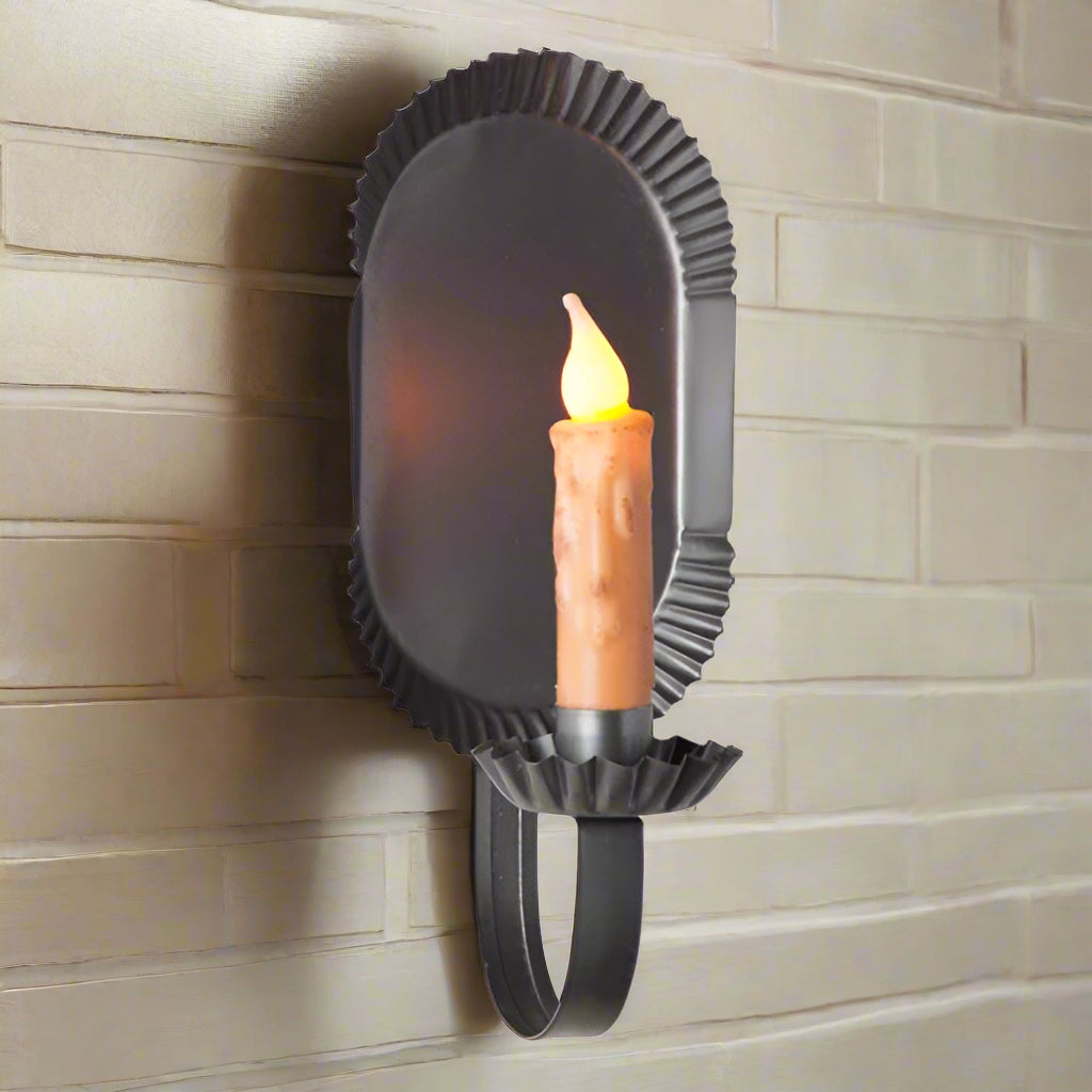 A black metal candle sconce with a smokey finish, designed to hold a candle. The sconce is shaped like a rounded tin with a handle at the bottom.