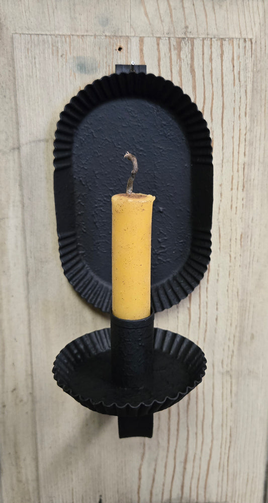 A black metal candle sconce mounted on a wall, holding a yellow taper candle.