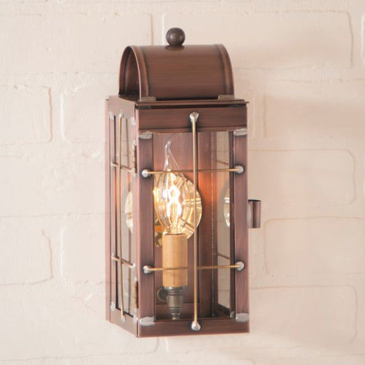 Antique copper wall lantern with clear glass and a visible wick, mounted on a white brick wall.
