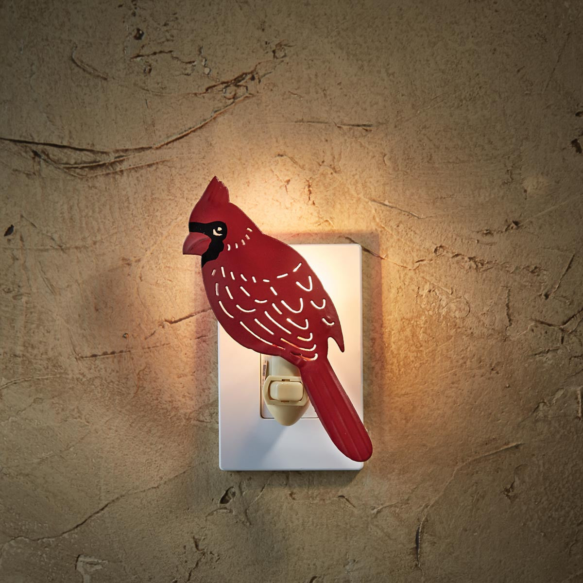 A red and black cardinal bird night light mounted on a white wall socket, illuminated with a warm light.