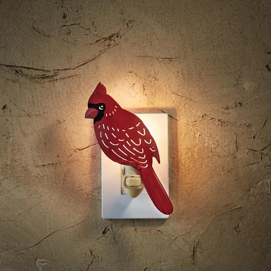 A red and black cardinal bird night light mounted on a white wall socket, illuminated with a warm light.