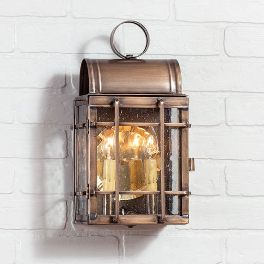 A solid weathered brass outdoor wall light with a 2-light design, hanging on a white brick wall.