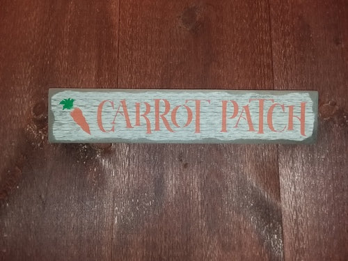A wooden sign with a carrot patch logo in orange, surrounded by a green border, placed on a wooden surface.