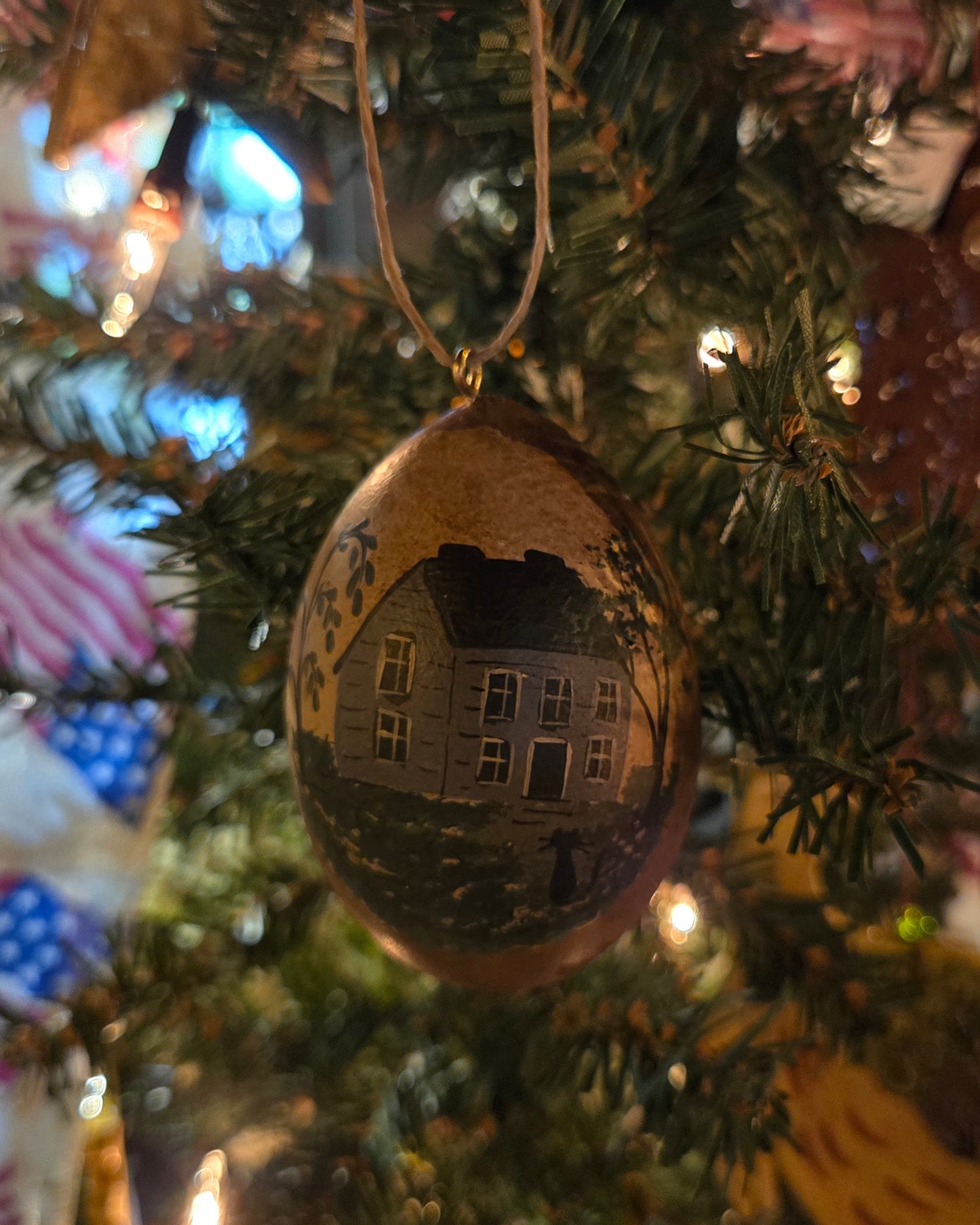 A handcrafted gourd ornament with a painted house design, hanging on a Christmas tree.