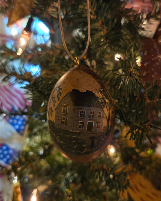 A handcrafted gourd ornament with a painted house design, hanging on a Christmas tree.