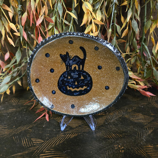 Decorative pottery with a black cat design surrounded by leaves.