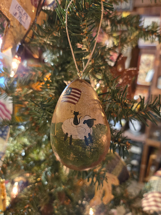 A handcrafted gourd ornament with a painting of a sheep and a flag, hanging on a Christmas tree.