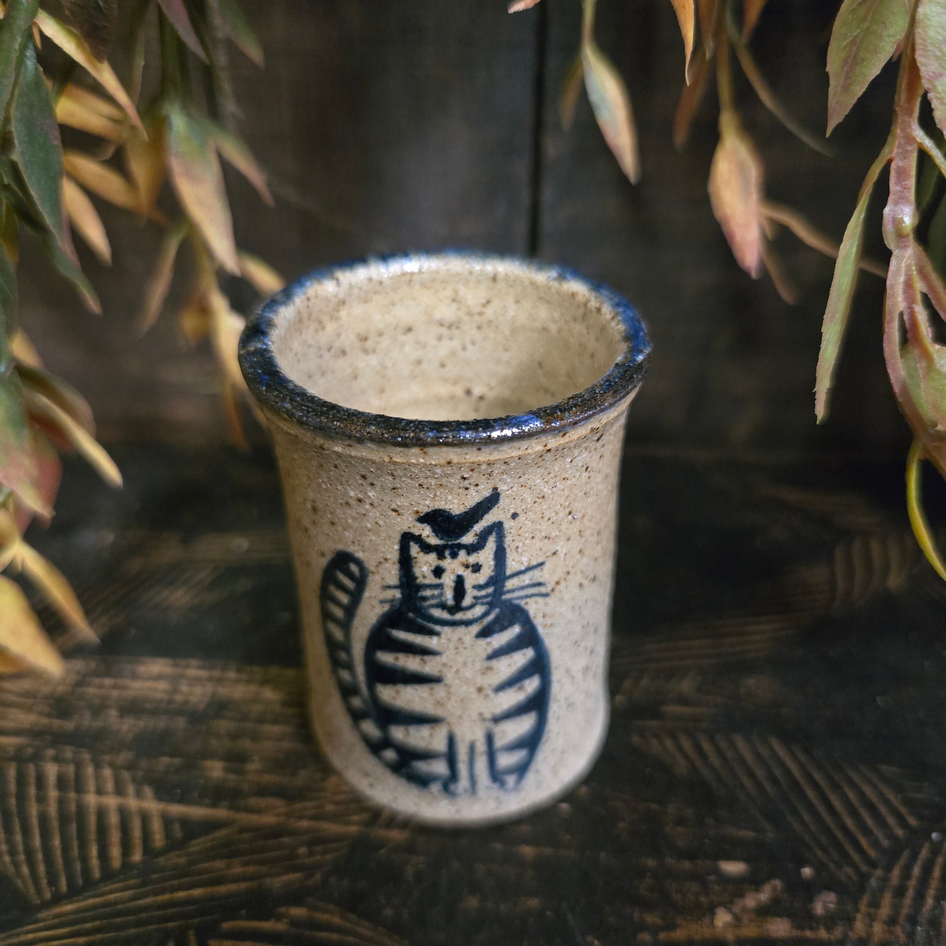 Ceramic cup with a cat design on a textured surface with plants.