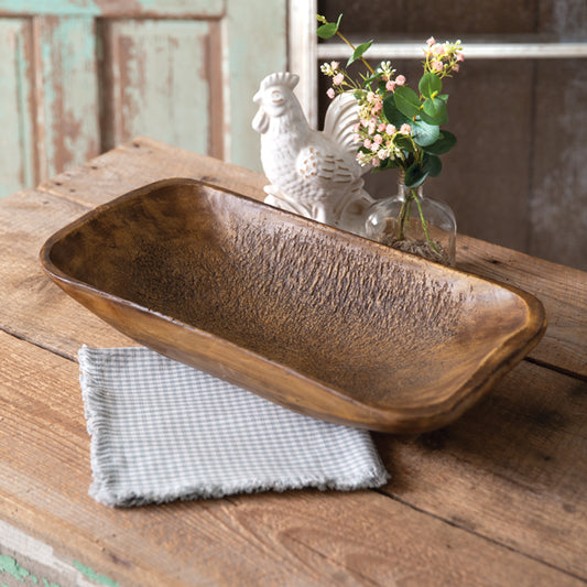 A brown rectangular centerpiece bowl made of resin, displayed on a wooden surface with a checkered napkin and decorative items in the background.