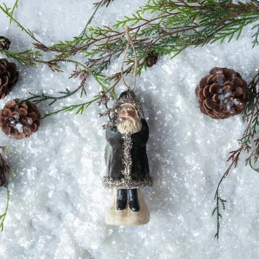 Decorative ornament of a person in a coat with greenery and pinecones on a snowy background