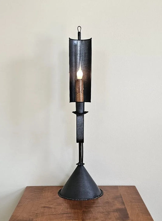 Black metal candle holder with a lit candle on a wooden surface against a white wall