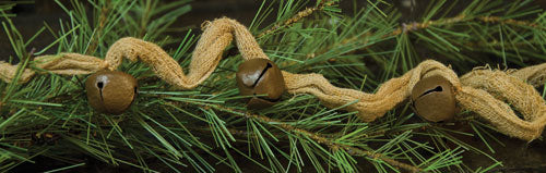 A close-up of a beige cheesecloth garland with bell accents, set against a blurred green pine background.