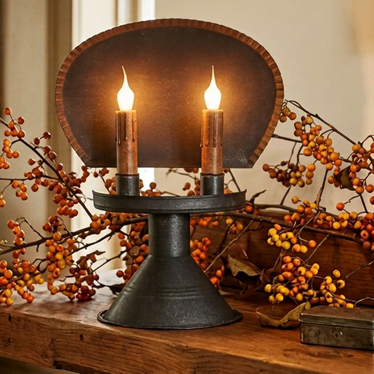 A Chesapeake Tin Table Light with two lit candles on a wooden surface, showcasing its sleek design and black color.