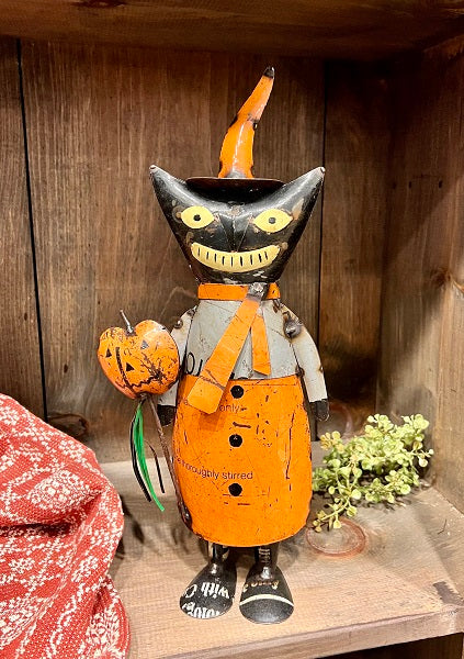 Halloween-themed figurine with black cat face, orange overalls, and pumpkin on a wooden surface.