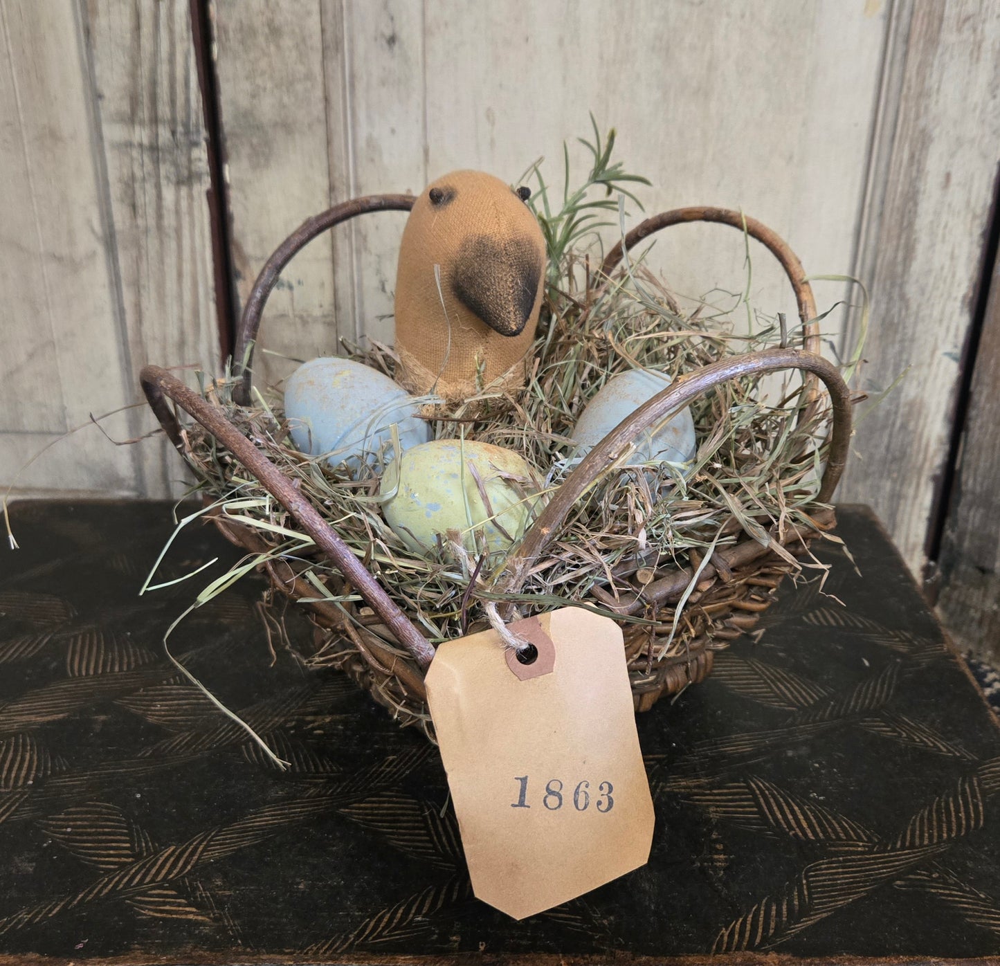 Decorative Easter basket with eggs, a bird figurine, and a '1863' tag on a wooden surface.