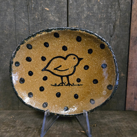 Round ceramic dish with black polka dots and a bird design on a wooden surface