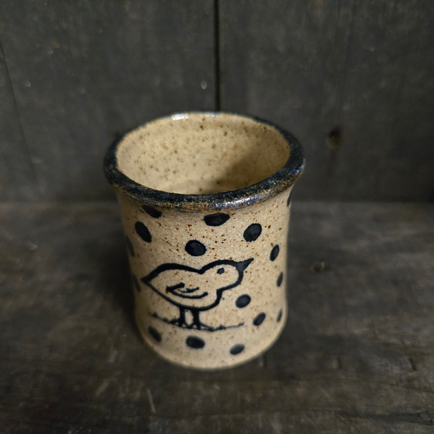 Ceramic cup with black speckles and a bird design on a dark wooden surface