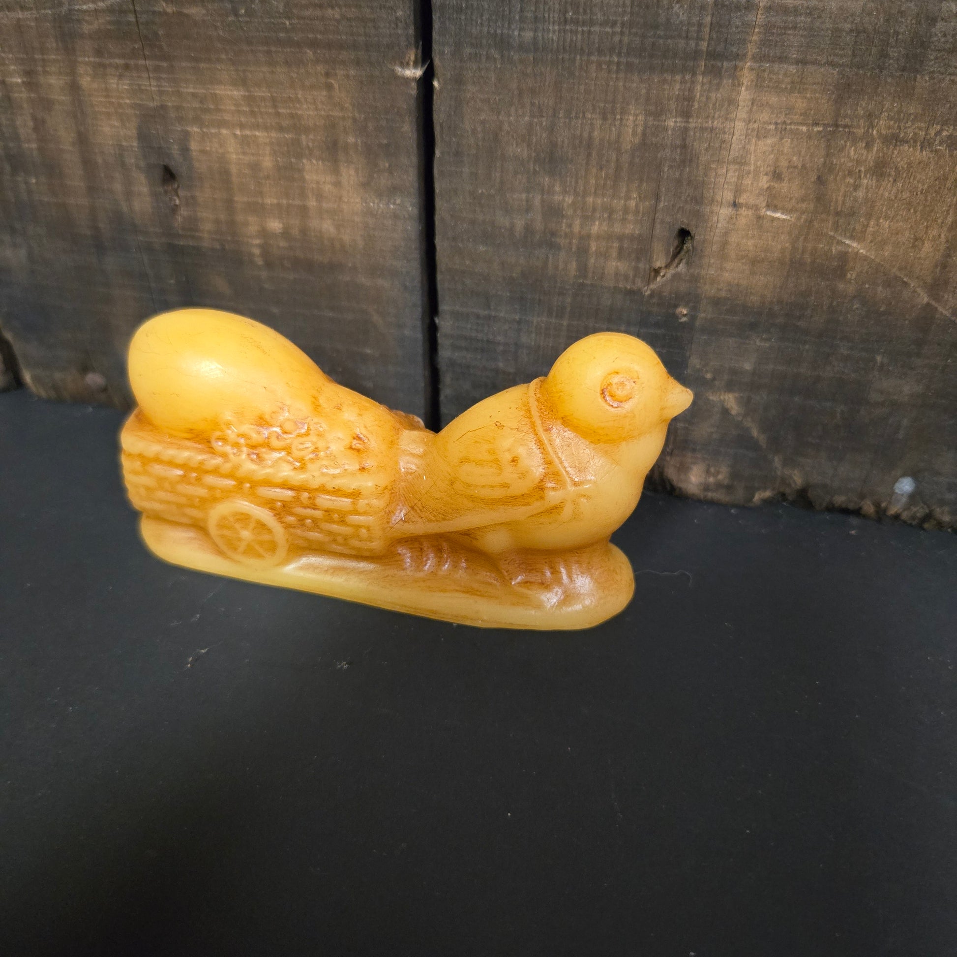 Beeswax chick with egg wagon on a dark wooden surface