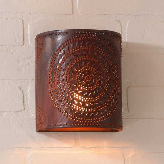 Decorative wall sconce in rusty tin finish with embossed design on a light brick wall.