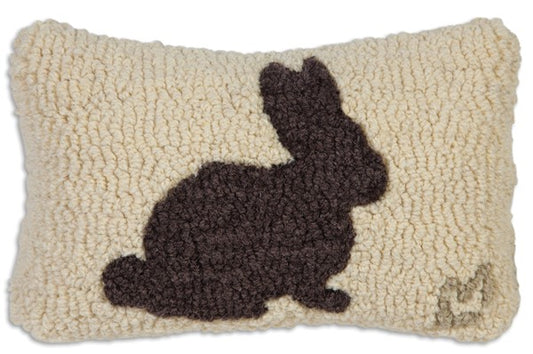 A hooked wool pillow with a design of a chocolate bunny on a beige background, with a velveteen backing.