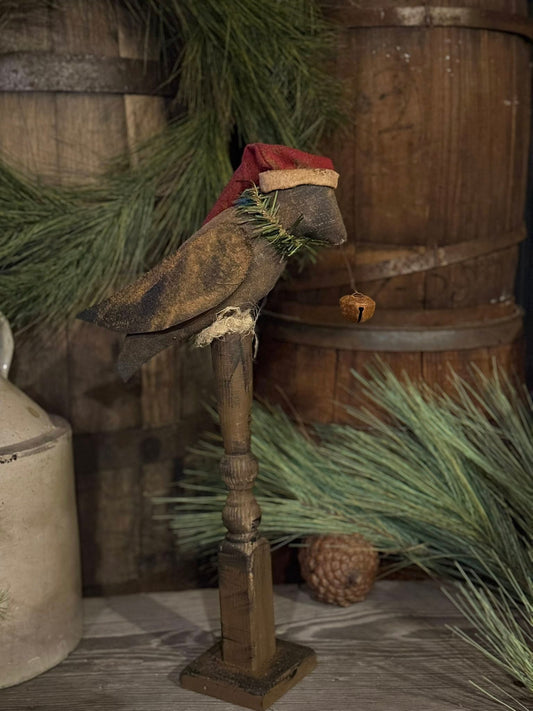 Decorative wooden stand with a crow wearing Santa hat and greenery against a rustic wooden background