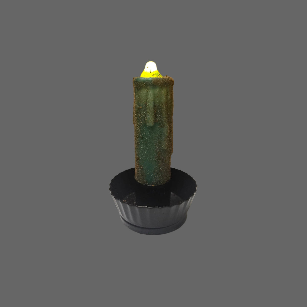A single green candle-shaped product with a black base, photographed on a white surface with a brown corrugated cardboard backdrop.