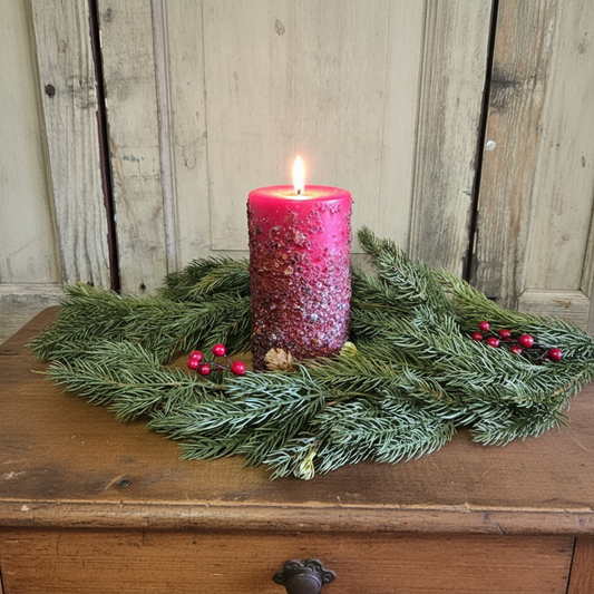 Pink candle on a bed of greenery with berries against a wooden background
