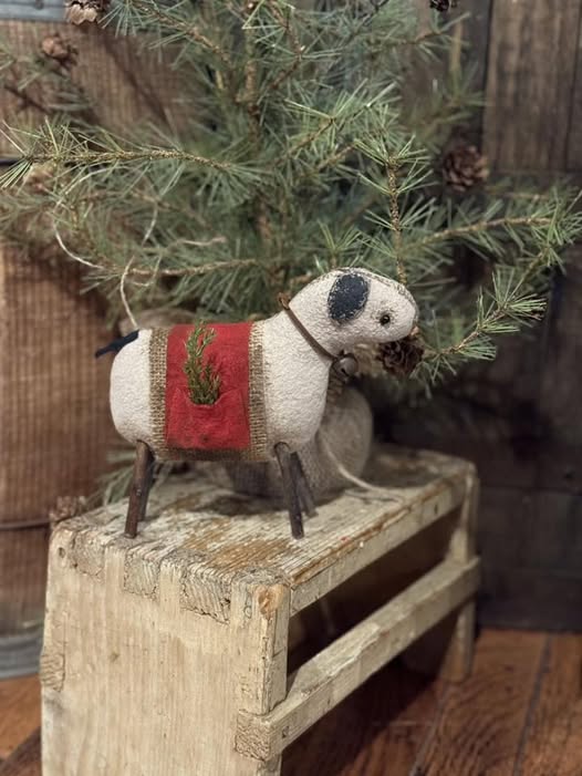 Decorative sheep figurine with a red blanket in front of a Christmas tree.