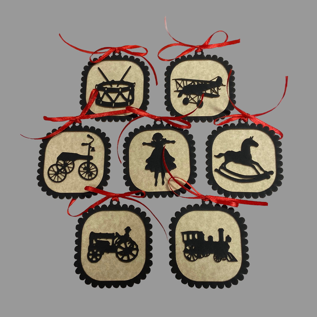 Set of 7 Christmas ornaments with silhouette designs of various toys, each with a red ribbon hanger.