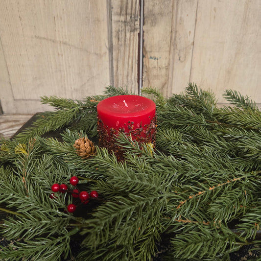Green wreath with red candle and berries against a wooden wall