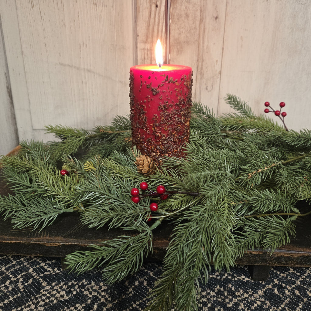 Red pillar candle with greenery and berries against a wooden background