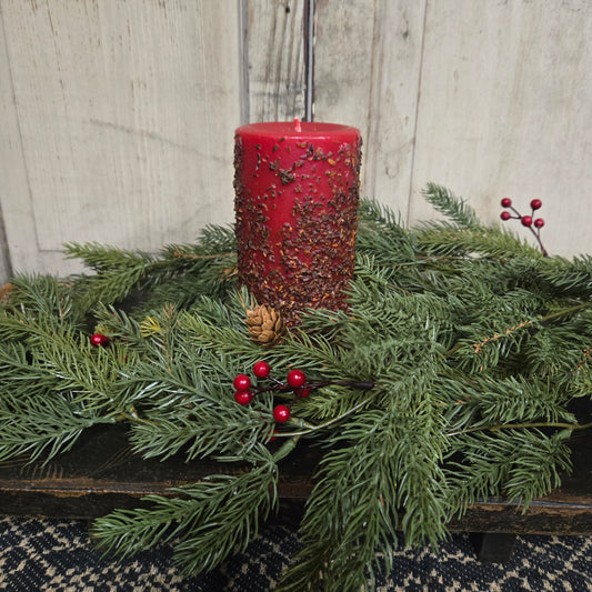 Red bird feeder attached to a branch with greenery and berries against a wooden background