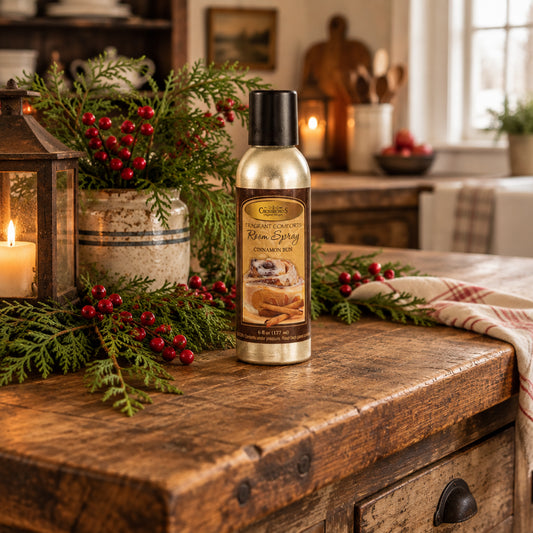 A 6 fl oz can of Cinnamon Bun room spray by CrispinRud's Fragrant Comforts, featuring a metallic gold body, a dark brown label with a cinnamon bun illustration, and a black cap, set against a plain white background.