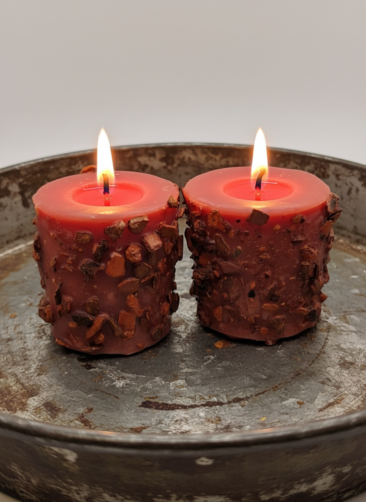 Two lit red candles with textured holders on a metal surface.